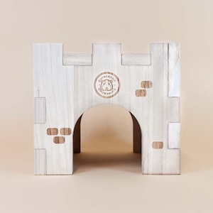 May include: White wooden castle-shaped hideaway for small pets, featuring a rounded archway entrance and a GuineaDad logo.