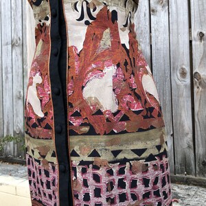 May include: A patterned dress with a button-up front. The dress features a mix of colors, including orange, brown, and black, with a geometric and floral design. The dress has a black trim and buttons.