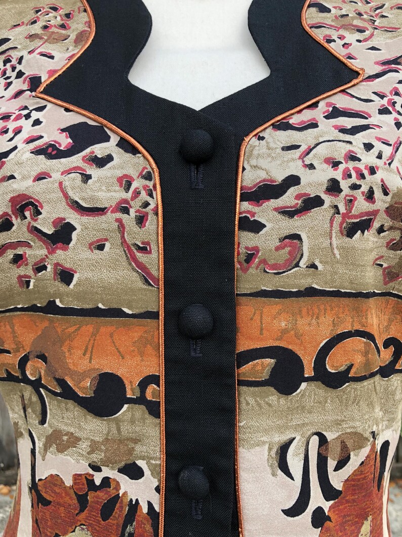 May include: Close-up of a vintage patterned jacket. The jacket features a beige, brown, and red abstract design. It has a black collar and button closure, with a thin orange trim. The jacket is a unique piece of vintage apparel.