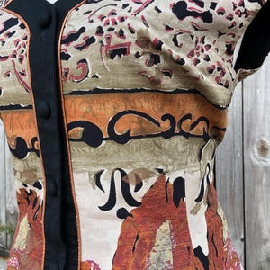 May include: A sleeveless top with a unique pattern in shades of brown, orange, and black. The top features a black trim and buttons down the front. The fabric has a vintage look with an abstract design.