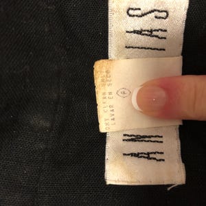 May include: Close-up of a black fabric with two white labels. One label reads "SAYI" in black capital letters. The other label is a care instruction tag with the words "DRY CLEAN ONLY" and "LAVAR EN SECO".
