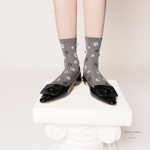 May include: Gray sheer socks with a small white and black flower pattern. The socks are worn with black leather flats with a large black buckle.