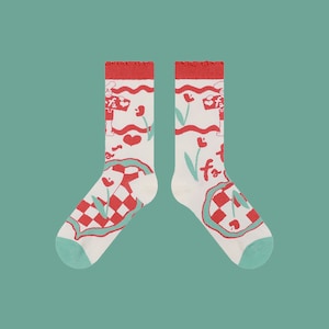 May include: A pair of white socks with a red and green checkered pattern and a whimsical design featuring a cartoon character, hearts, and flowers.