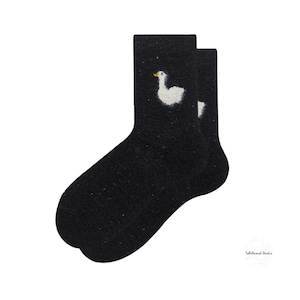 May include: A pair of black fuzzy socks with a white goose design. The goose has a yellow beak and is embroidered on the socks.