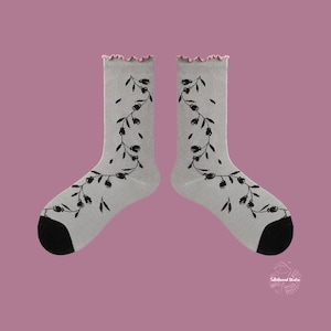 Flat lay of Wildflower Vine socks in soft grey with black botanical prints and a pink scalloped cuff on a dusty rose background