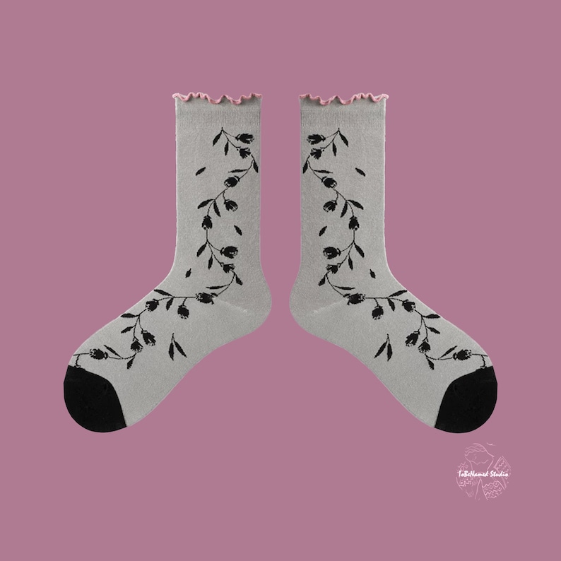 Flat lay of Wildflower Vine socks in soft grey with black botanical prints and a pink scalloped cuff on a dusty rose background