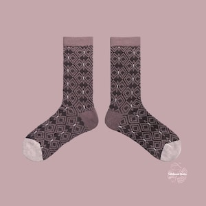 May include: A pair of patterned socks. The socks have a repeating diamond design in shades of brown and white, with a mauve cuff, heel, and toe. The background is a solid mauve colour.