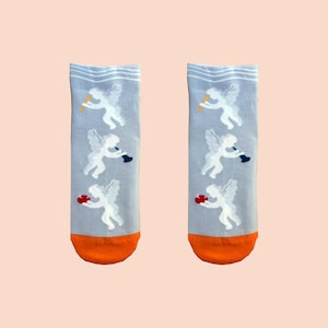 May include: A pair of gray socks with a white design of cherubs playing musical instruments and holding hearts. The socks have orange trim.