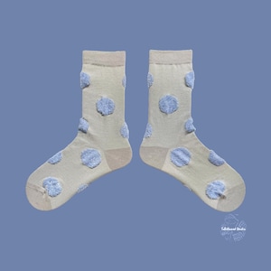 Puede incluir: Un par de calcetines beige con lunares azules claros texturizados. Los calcetines tienen talón y puntera marrón claro, y un puño marrón claro. Los calcetines se muestran sobre un fondo azul. Un accesorio divertido y elegante.