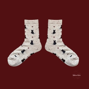 May include: A pair of light gray socks with a pattern of black cat silhouettes and small red hearts. The socks are displayed against a dark red background, showcasing the whimsical design.
