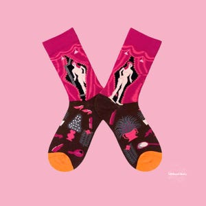 May include: A pair of brown and pink socks with a colourful design featuring a woman standing in a doorway. The socks have a variety of other designs including flowers, a comb, and a mirror.