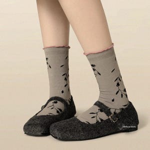 Close-up of legs wearing grey vine-print socks with a pink lettuce-edge top, paired with dark grey Mary Jane shoes