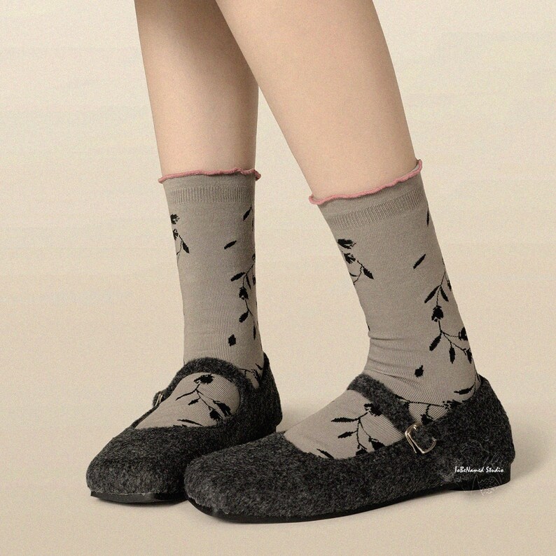 Close-up of legs wearing grey vine-print socks with a pink lettuce-edge top, paired with dark grey Mary Jane shoes