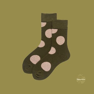 May include: A pair of olive green socks with large, light pink polka dots. The socks are made of a soft material and have a ribbed cuff. The background is a solid olive green.