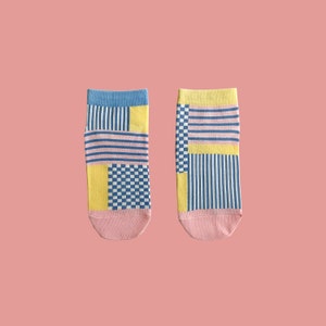 Puede incluir: Un par de calcetines con un patrón geométrico en tonos de azul, amarillo y rosa. Los calcetines tienen un patrón a cuadros, rayas y colores sólidos.