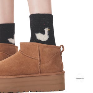 May include: A pair of brown suede ankle boots with a thick platform sole. The boots are worn with black socks featuring a white embroidered duck design.