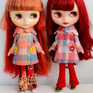 May include: Two dolls with long red hair wearing plaid coats and bell bottom pants. The doll on the left has orange hair and is wearing floral pants. The doll on the right has red hair and is wearing red and black polka dot pants. The dolls are labeled "Orange" and "Red".