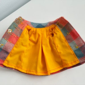 May include: A red, blue, and gray plaid skirt with a yellow lining. The skirt has a gathered waist and is lined with a yellow fabric.