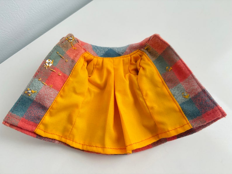 May include: A red, blue, and gray plaid skirt with a yellow lining. The skirt has a gathered waist and is lined with a yellow fabric.