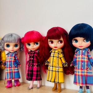 May include: Four dolls with large eyes and distinct hair colors, including silver, pink, red, and dark blue. Each doll wears a long-sleeved, button-down plaid coat featuring decorative bead accents on the pockets and cuffs, paired with matching footwear.