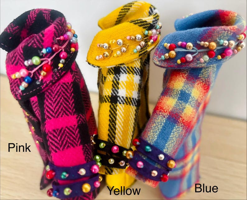 May include: Three miniature coats in pink, yellow, and blue plaid patterns. Each coat features a collar and cuffs embellished with colorful beads. The text Pink, Yellow, and Blue is printed below the respective coats to identify each color variant.