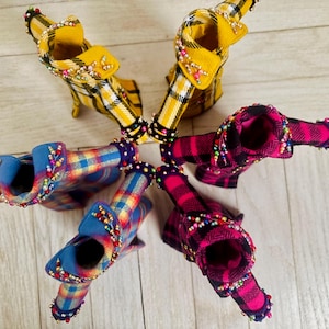 May include: Five miniature jackets arranged in a circle, featuring two yellow plaid, two pink and black plaid, and one blue and yellow plaid design. Each jacket is embellished with small, colorful beads along the collars and sleeve cuffs.