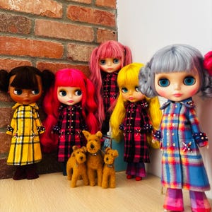 May include: Five dolls with large eyes and distinct hair colors wearing plaid coats with beaded accents, accompanied by three small brown felted dog figures. The dolls have hair in shades of dark brown, bright pink, yellow, and light blue.