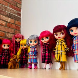 May include: A collection of eight dolls standing in a row, wearing various plaid coats in yellow, blue, and pink. The dolls feature diverse hair colors including pink, yellow, silver, red, and dark blue, and are positioned on a flat surface.
