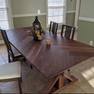 May include: A dark wood dining table with a chevron pattern top and a trestle base. The table is set with candles and a floral centerpiece.