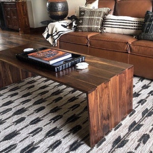 May include: A dark wood coffee table with a black tray and a book on top. The table is sitting on a white and black patterned rug.