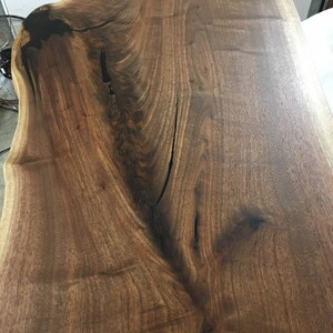 May include: A close-up of a large, dark brown wood slab with a natural edge. The wood has a rich grain pattern and a smooth, polished finish.