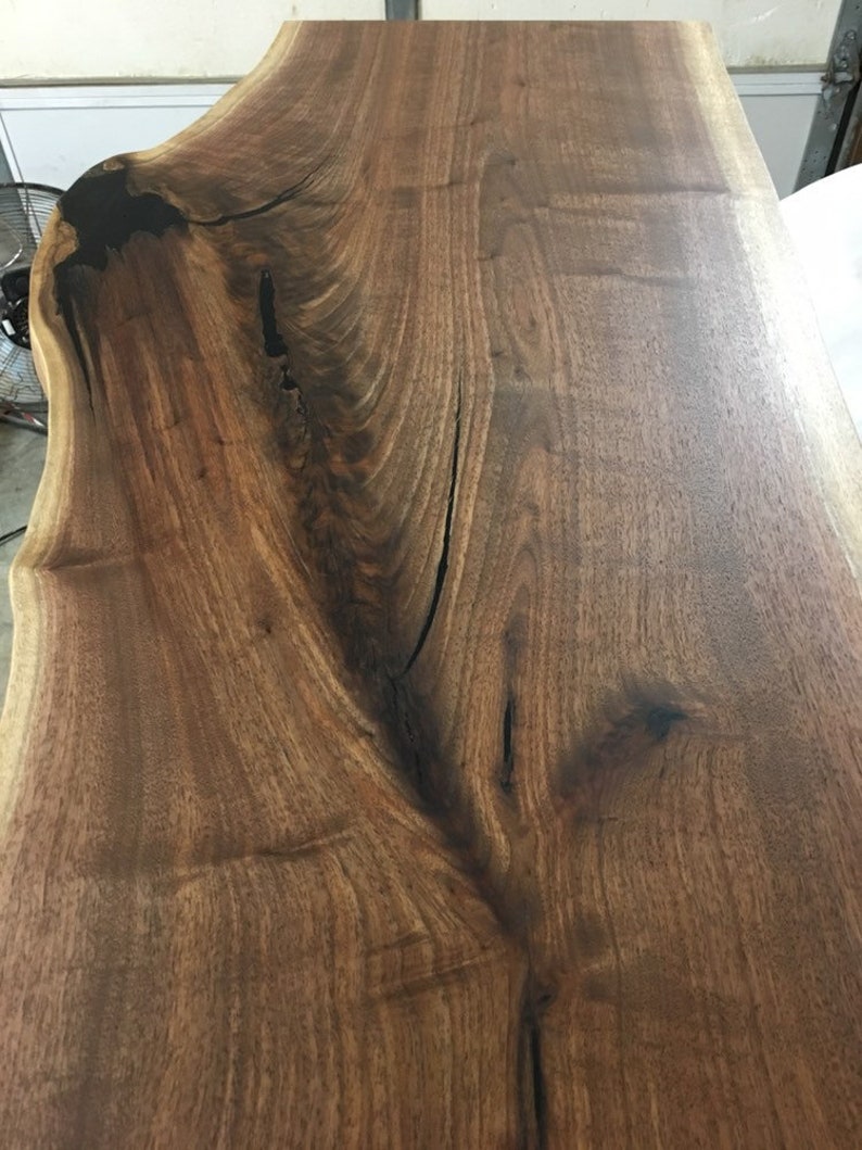 May include: A close-up of a large, dark brown wood slab with a natural edge. The wood has a rich grain pattern and a smooth, polished finish.