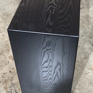 May include: A black wooden bench with a smooth, polished finish. The grain of the wood is visible and adds a natural texture to the piece.