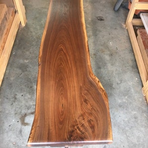 May include: A large, dark brown wooden slab with a live edge. The wood has a natural grain pattern and is polished to a smooth finish.