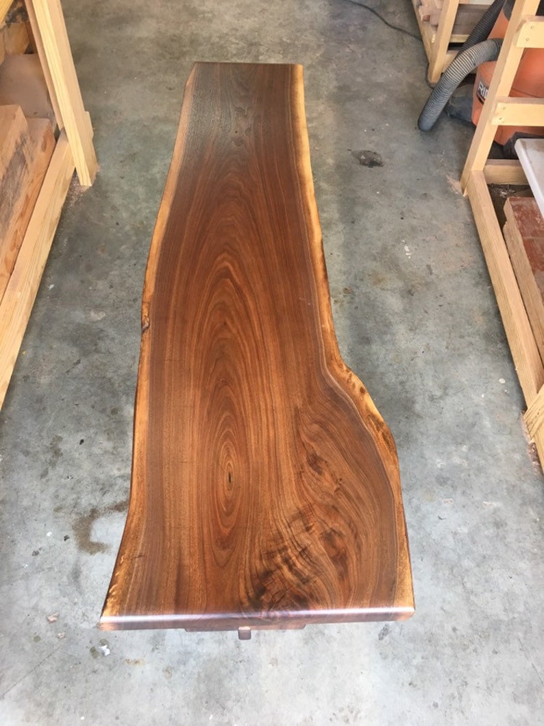 May include: A large, dark brown wooden slab with a live edge. The wood has a natural grain pattern and is polished to a smooth finish.