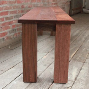 May include: A wooden bench with a dark brown finish. The bench has four legs and a rectangular top.
