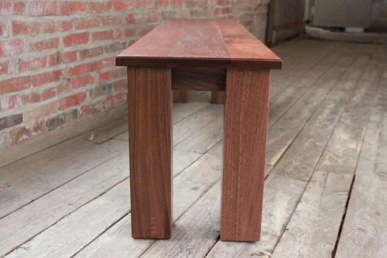 May include: A wooden bench with a dark brown finish. The bench has four legs and a rectangular top.
