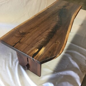 May include: A live edge walnut wood coffee table with a natural finish. The table has a unique shape and is supported by two legs.