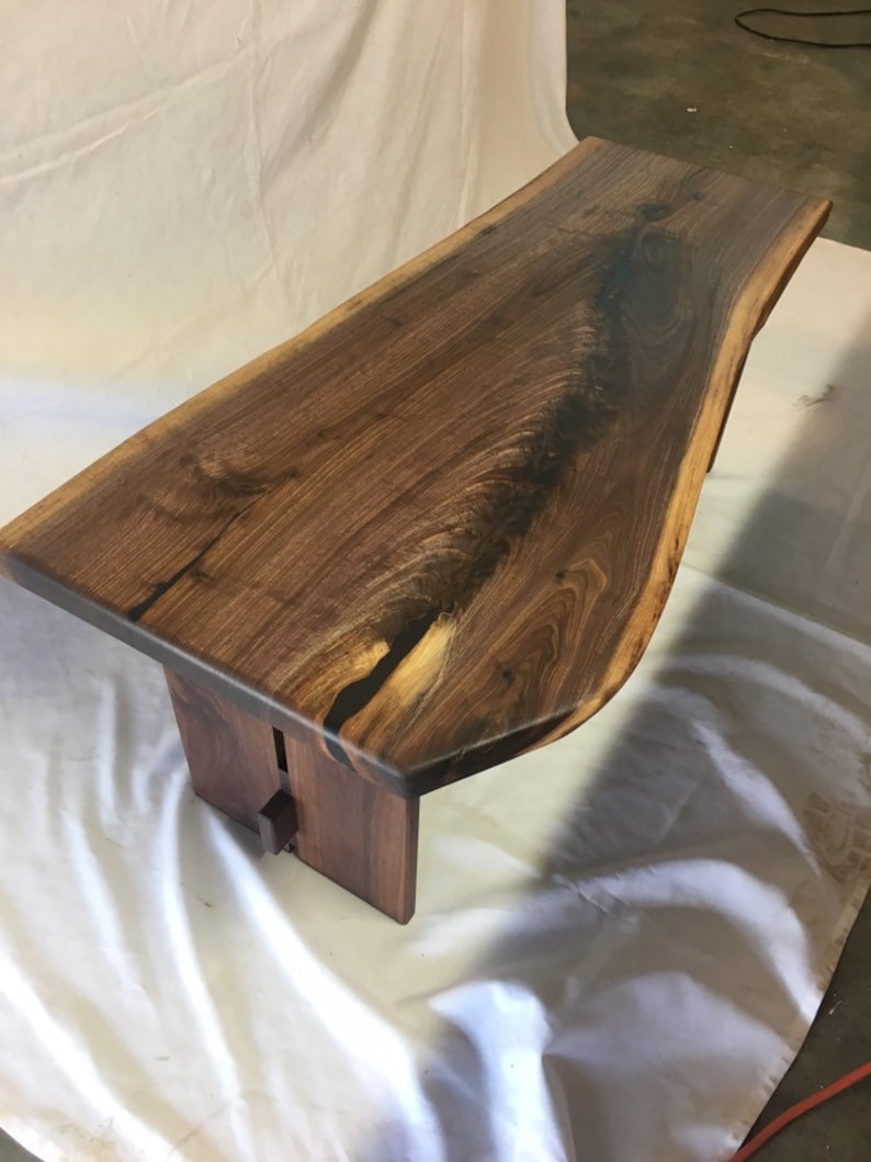 May include: A live edge walnut wood coffee table with a natural finish. The table has a unique shape and is supported by two legs.