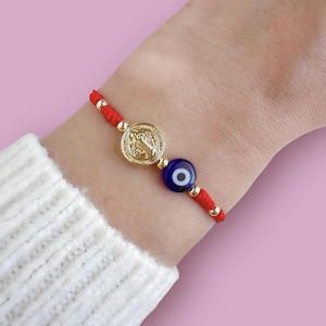 May include: Red string bracelet with a gold charm and a blue evil eye charm.