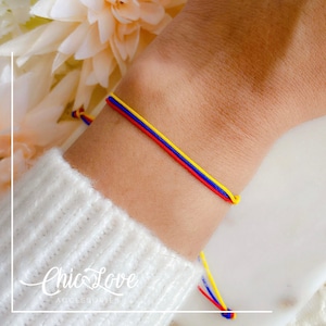 May include: A colorful friendship bracelet with blue, yellow, and red string. The bracelet is tied on a person's wrist.