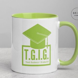 Könnte beinhalten: Weißer Keramikbecher mit grünem Innenraum und Griff. Der Becher zeigt eine grüne Abschlusskappe und den Text "T.G.I.G. Thank Goodness I Graduated" in einem grünen rechteckigen Rahmen. Der Becher hat das Logo "BRI+E STUDIO".