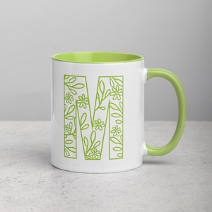Peut inclure: Tasse en céramique blanche avec intérieur et anse verts. La lettre "M" est affichée sur le devant, remplie d'un motif floral vert. Convient aux boissons chaudes ou froides.