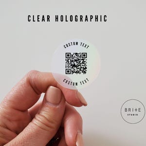 custom text 2 inch clear holographic qr code sticker shown against white background.