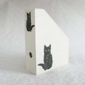 Peut inclure: Porte-revues en bois blanc orné d'illustrations de chats noirs aux yeux jaunes. L'art du chat est peint à la main sur le devant et le côté. Le support comporte un trou circulaire sur le côté.