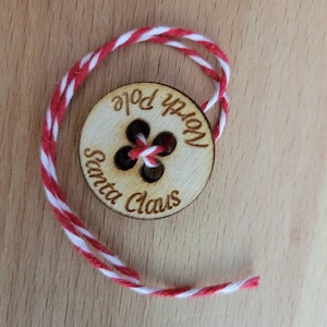 以下が含まれることがあります： 「North Pole Santa Claus」と書かれた木製のボタンと赤と白の紐