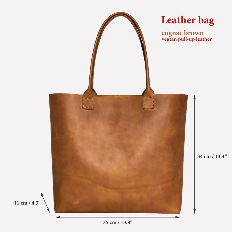 May include: A cognac brown leather tote bag with a vegan pull-up leather finish. The bag measures 35 cm wide, 34 cm tall, and 11 cm deep.