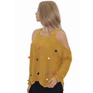 May include: A mustard yellow cold shoulder sweater with colourful pom poms.