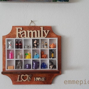 May include: A wooden wall shelf with the word "Family" in large letters on the top. The shelf has 16 small compartments, each containing a miniature object. The bottom of the shelf has the words "Love Home" carved into the wood.