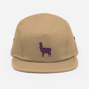Puede incluir: Una gorra de 5 paneles de color beige con un diseño de llama azul y rojo. La llama está estampada con círculos rojos sobre un fondo azul.